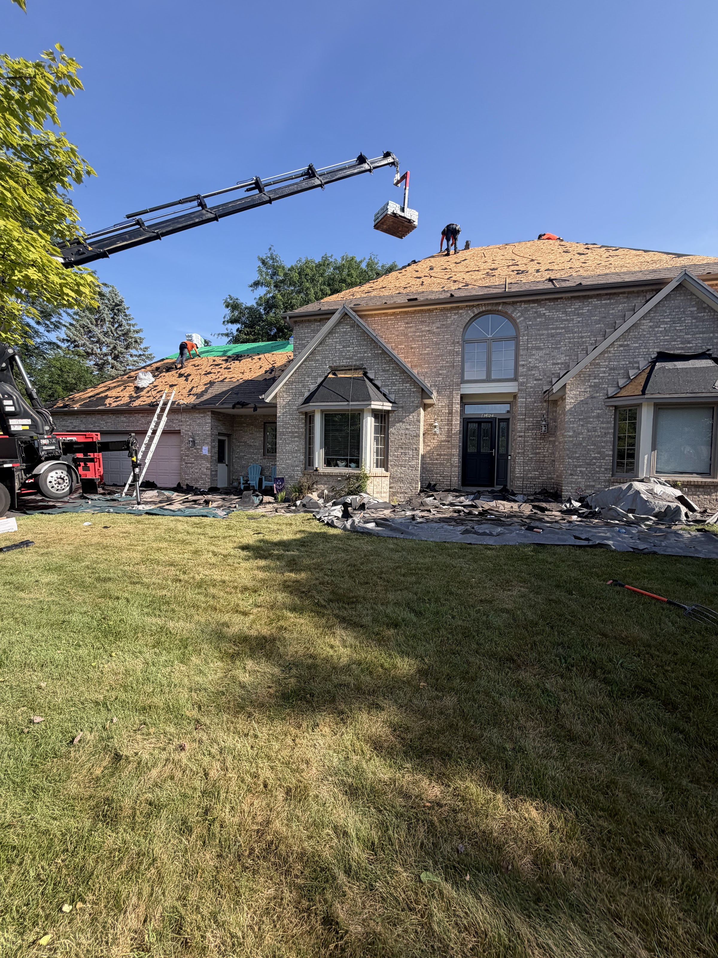 Full roof tear-off in progress on a large west metro home, with a materials conveyor truck staged out front and crew working the ridge