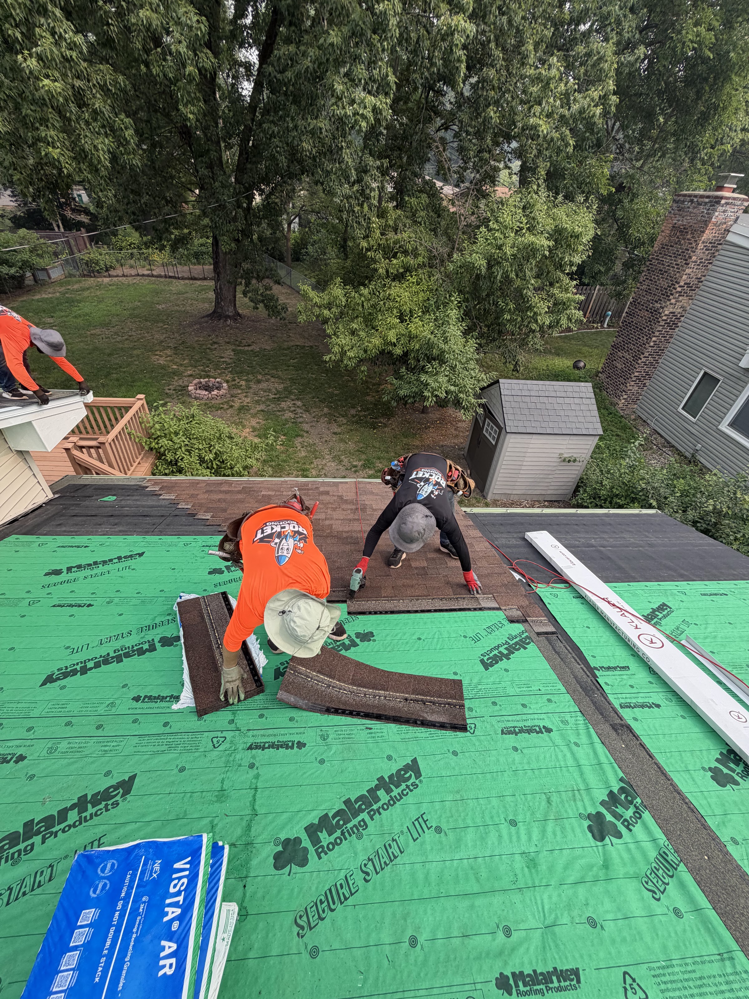 Three-person Rocket Roofing crew laying starter shingle courses over green synthetic underlayment